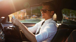 A man in a white shirt and blue tie grips the steering wheel.