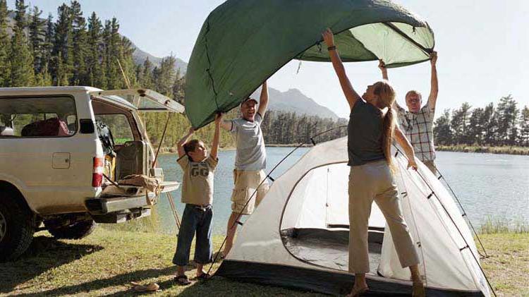 A family sets up a tent next to a lake.